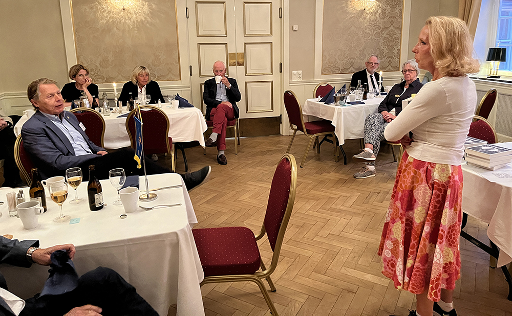 Författaren Thelma Kimsjö talar om sin roman Danssjukan inför blandad publik vid bord med vita dukar. Rotarylunch